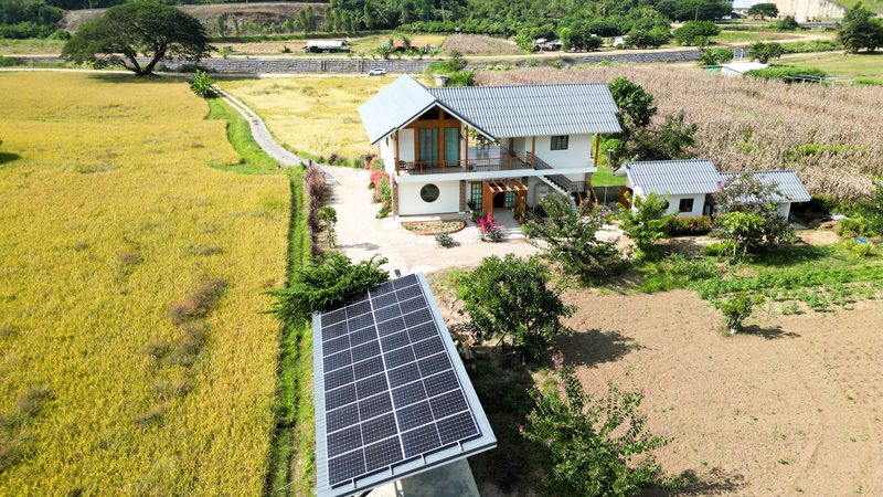 Ground-mounted solar array beside a farmhouse in rice fields near Mae Suai Dam